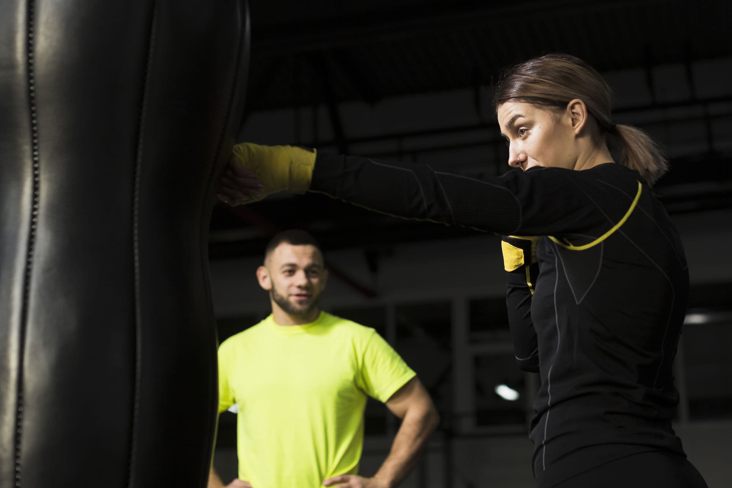 Mujer golpeando un saco de boxeo mientras su entrenador observa