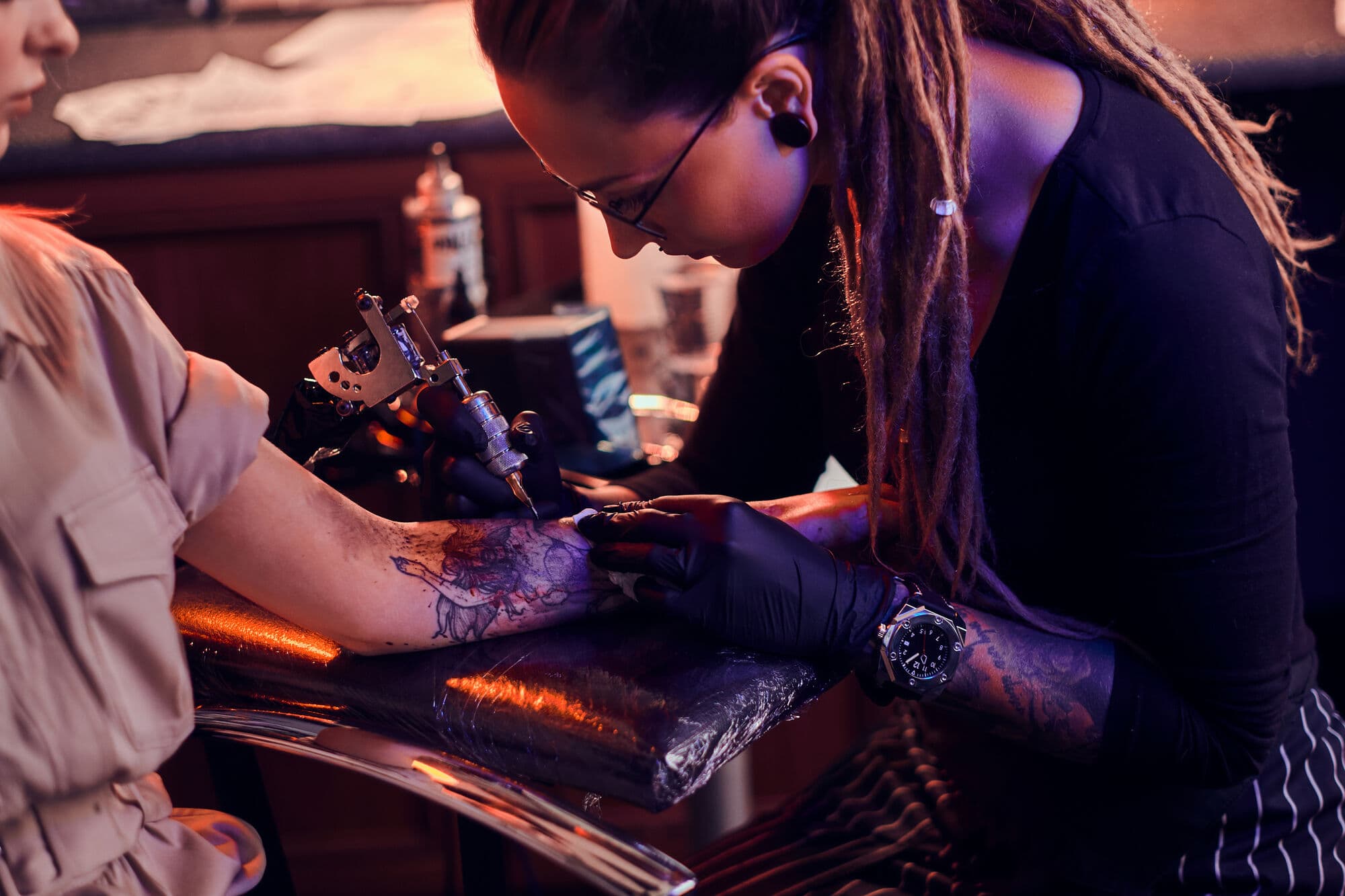 Tatuador trabajando en el brazo de un cliente en un estudio oscuro